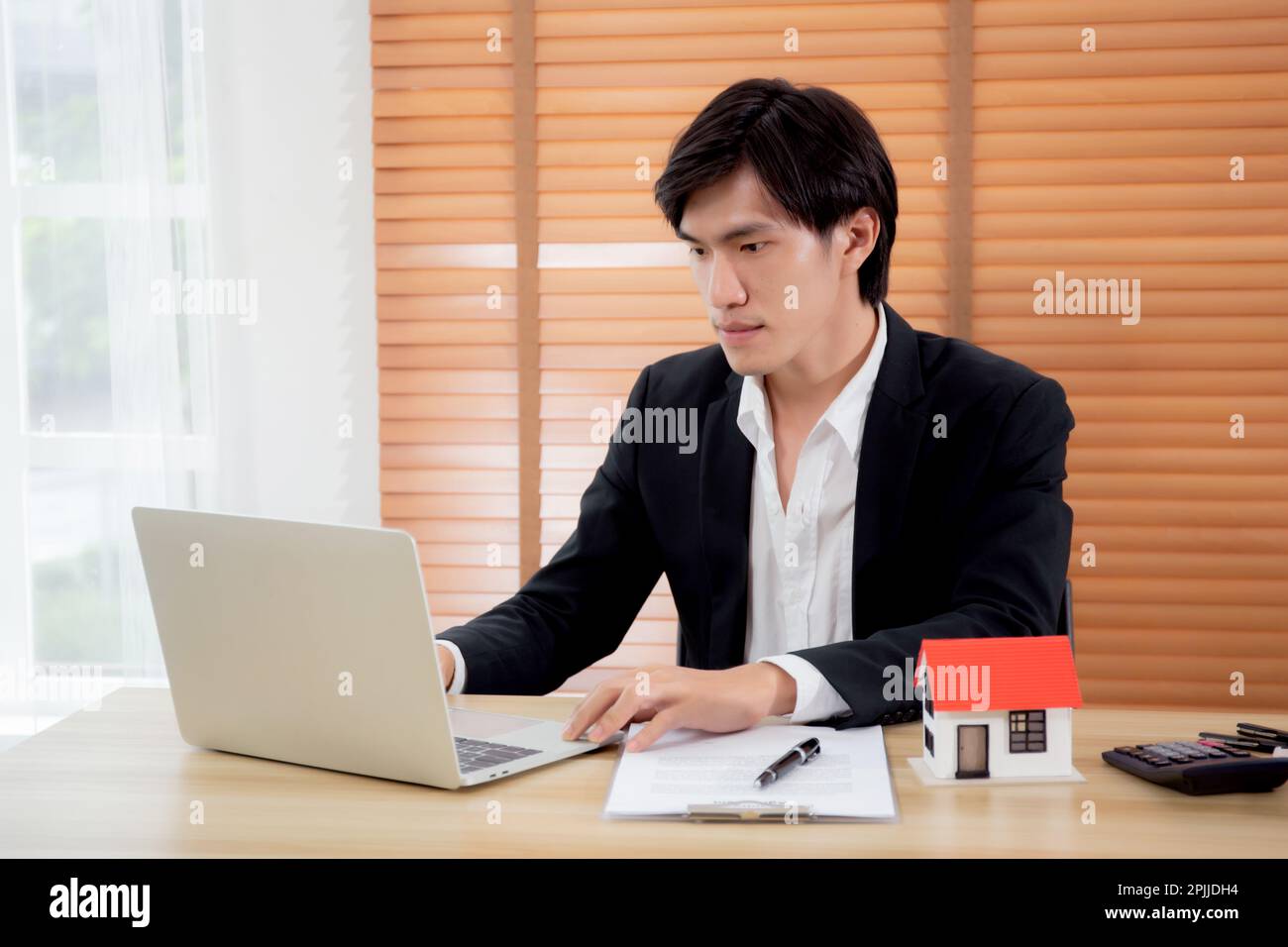 Giovane asiatico che utilizza il computer portatile mentre documenta sul contratto o la casa di assicurazione sulla scrivania, la pianificazione e la strategia sul bene immobile e l'investimento, Foto Stock