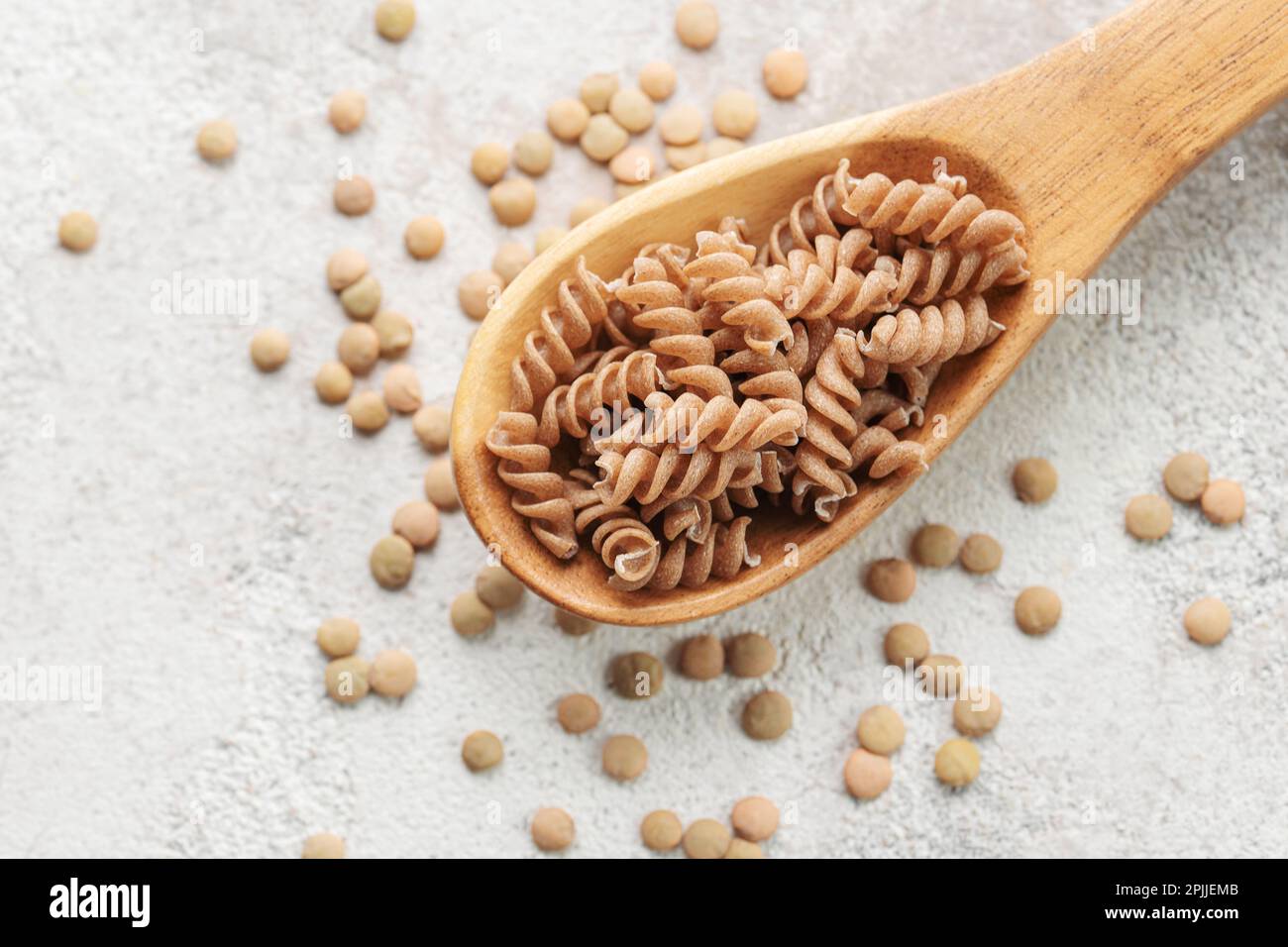 Lenticchie verdi fusilli su fondo grigio in cemento. Un cucchiaio di pasta cruda e lenticchie verdi. Pasta senza glutine. Foto Stock