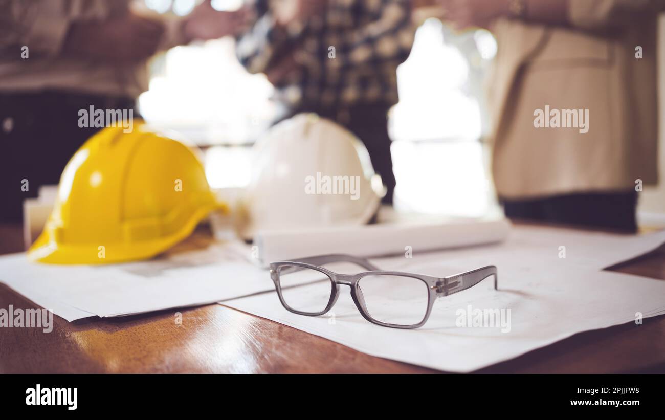 Vista ravvicinata del tavolo di lavoro del tecnico con occhiali, casco di sicurezza e BluePrint sulla scrivania nella sala ufficio. Foto Stock