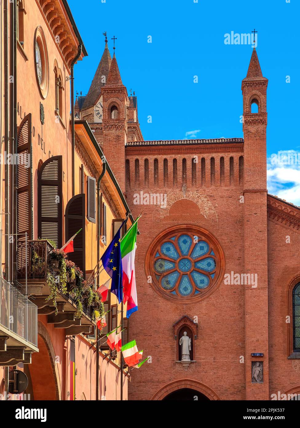Bandiere italiane sulla costruzione e la facciata della cattedrale di San Lorenzo sotto il cielo blu sullo sfondo della città di Alba, Piemonte, Italia settentrionale. Foto Stock