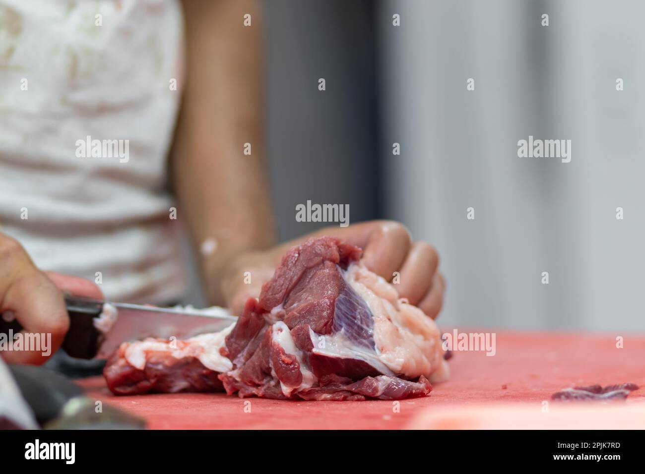 Un macellaio taglia a pezzi il manzo fresco, usando un coltello affilato. Sfondo sfocato Foto Stock
