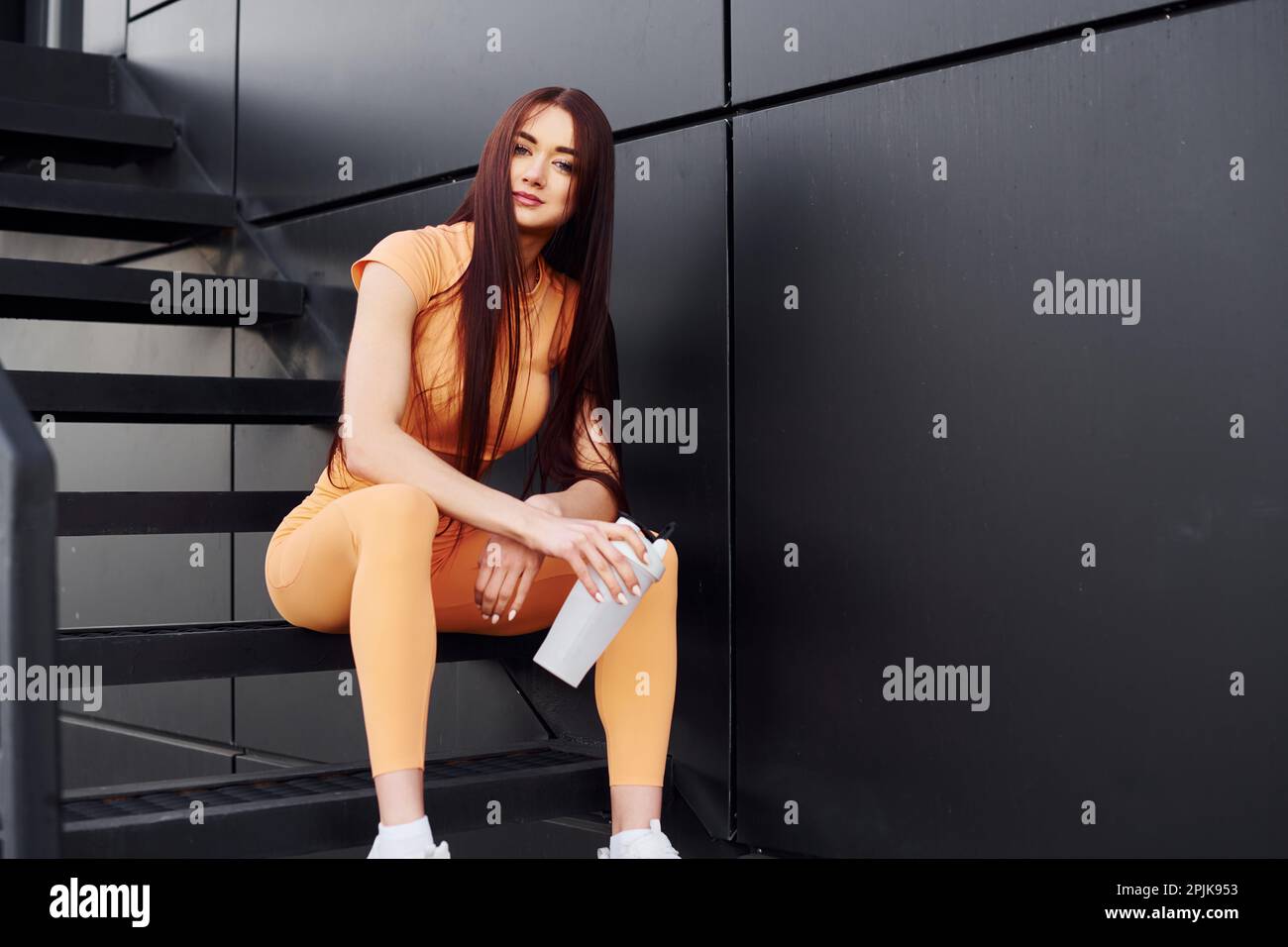Siede sulle scale e contiene una bottiglia d'acqua. Giovane donna in abbigliamento sportivo hanno sessione di fitness all'aperto Foto Stock