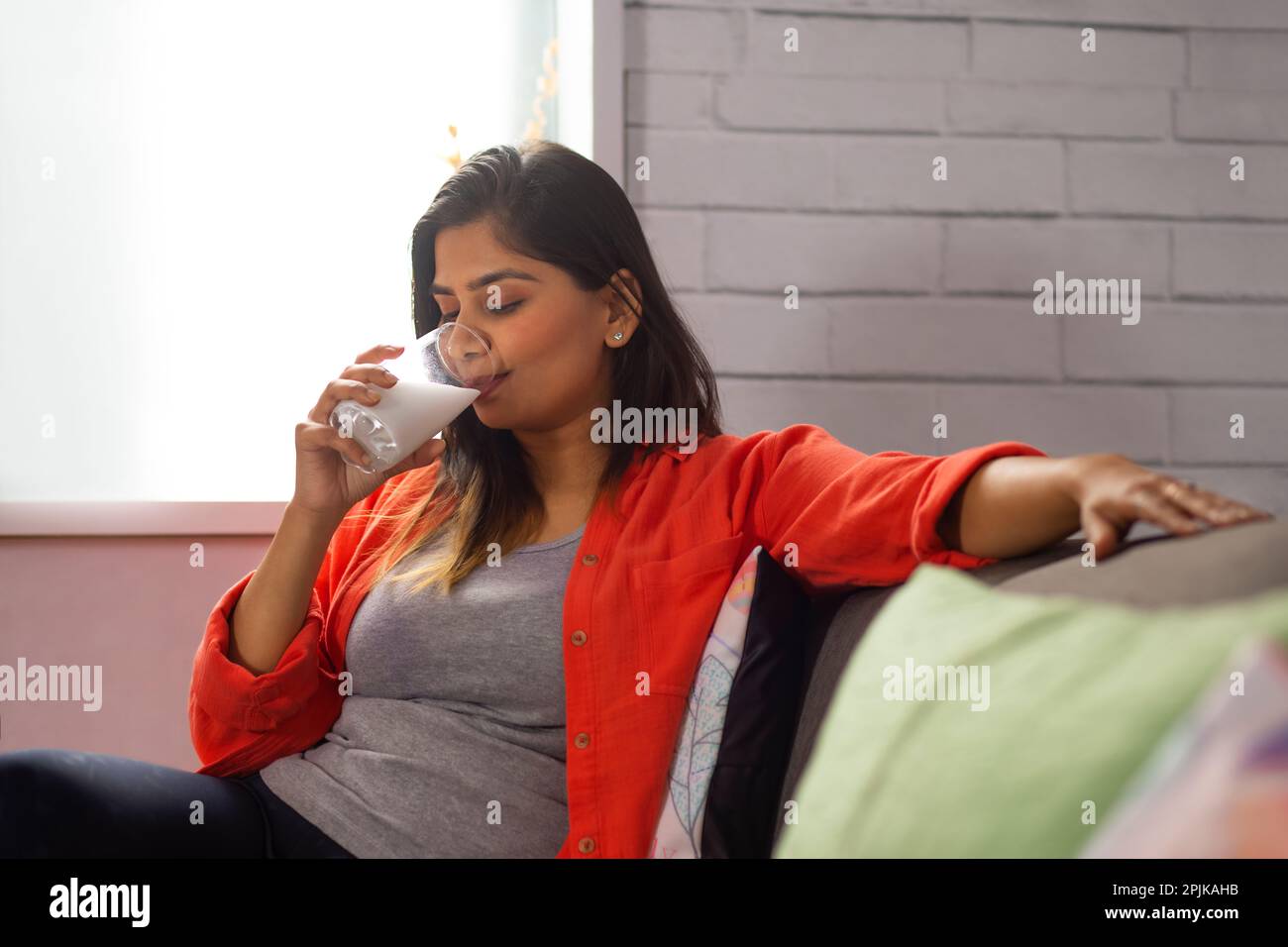 Donna che beve latte mentre si siede sul divano Foto Stock