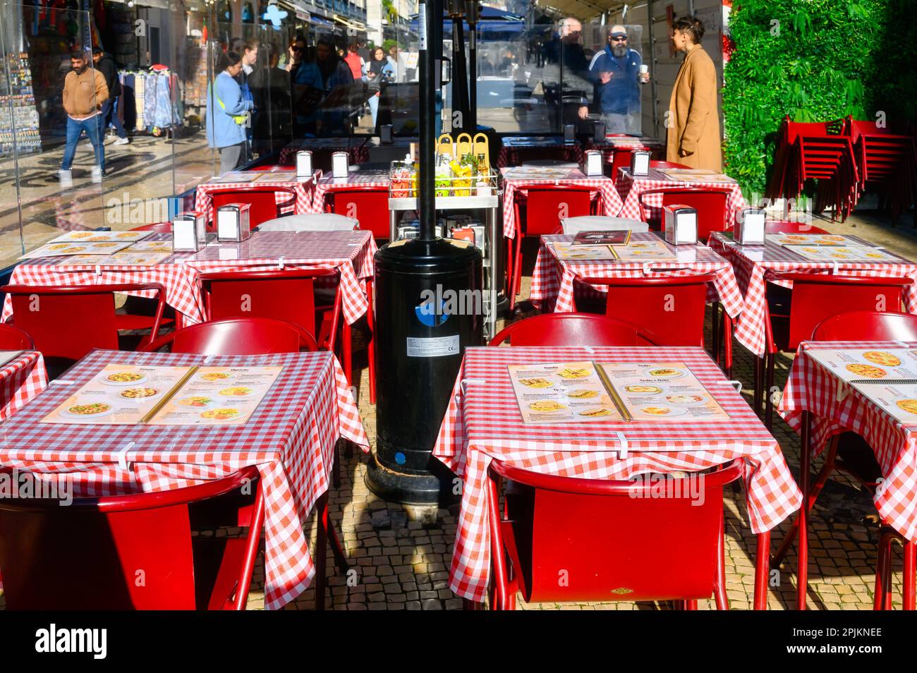 Lisbona, Portogallo - 4 gennaio 2023: Ristorante all'aperto con tavoli rossi e persone che camminano in background Foto Stock