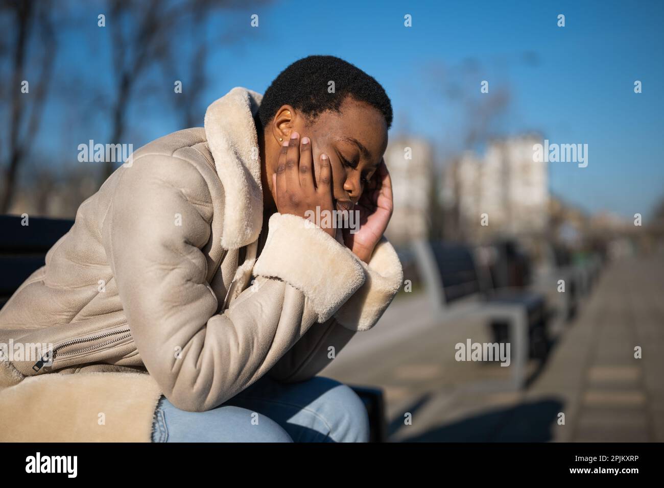 Ritratto all'aperto di depressa donna afro-americana in giornata di sole. È seduta su panca per strada. Foto Stock