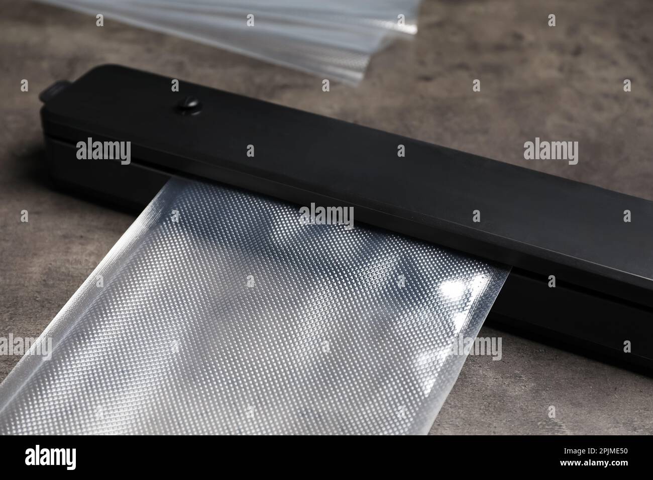 Sigillante per confezionamento sottovuoto con sacchetto di plastica su tavolo grigio, closeup Foto Stock