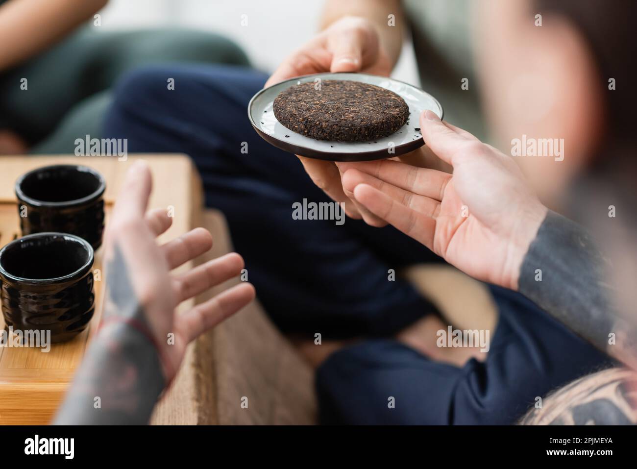 vista ritagliata dell'uomo tatuato che prende il piatto con il tè puer compresso e fermentato, immagine stock Foto Stock