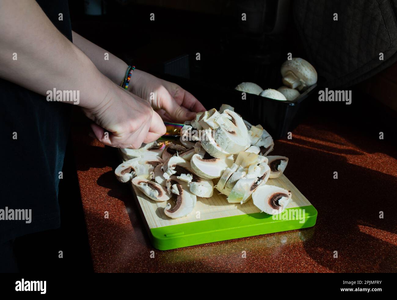 Primo piano delle mani con funghi freschi tagliati su un tagliere. Cucina vegetariana fatta in casa. Luce solare dalla finestra, ombre sul tavolo. Foto Stock
