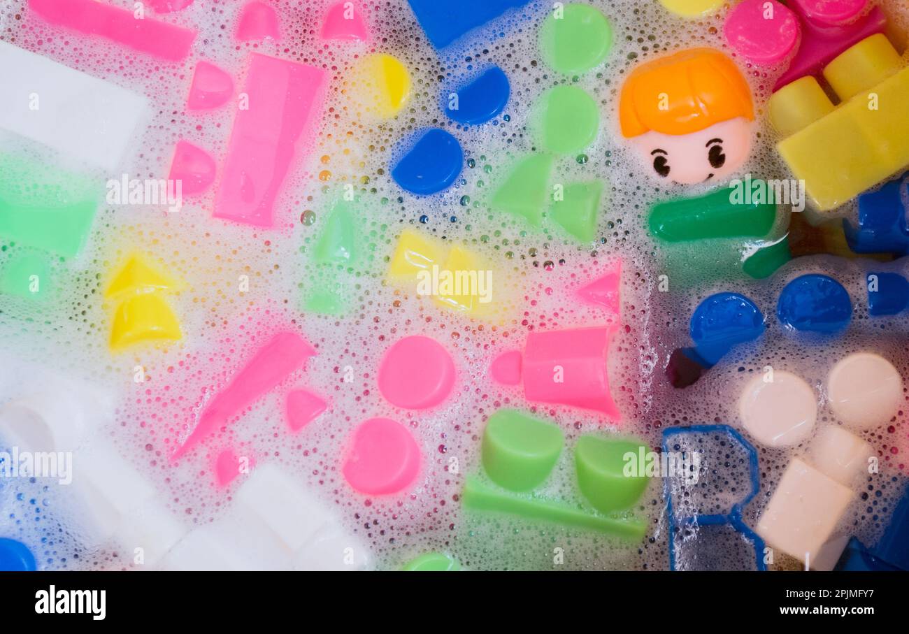 Lavaggio di giocattoli per bambini, blocchi da costruzione in plastica con figurine. Un piccolo compagno sorridente e cubi colorati galleggiano nell'acqua schiumosa. Il concetto o Foto Stock