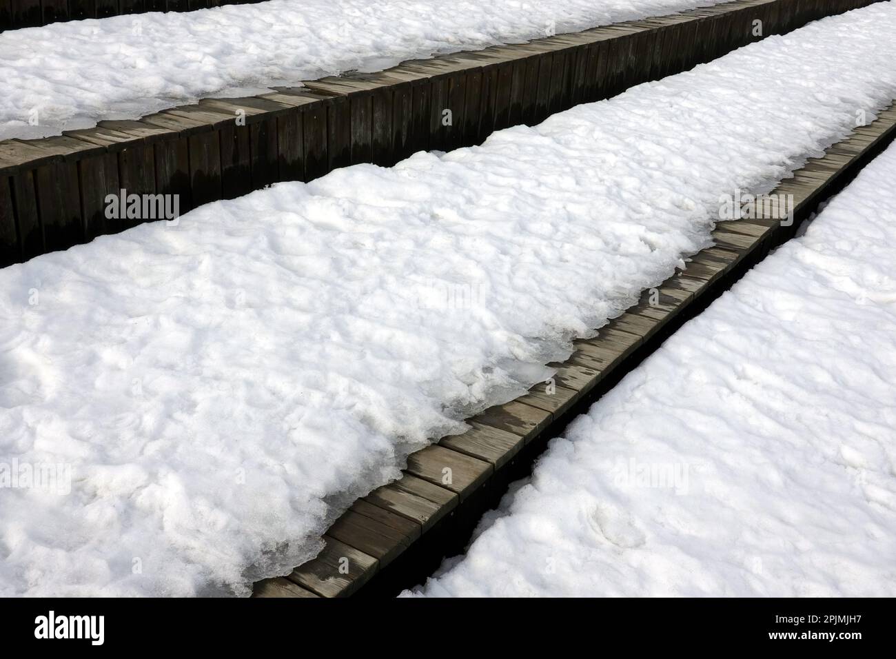 Fusione sulla neve primaverile sulle diverse superfici di vecchie tavole di legno marrone superficie esterna vista laterale primo piano Foto Stock