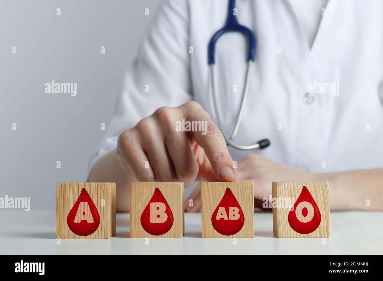 Cubi di legno con immagini di gocce che rappresentano diversi tipi di sangue e medico a tavola, primo piano Foto Stock