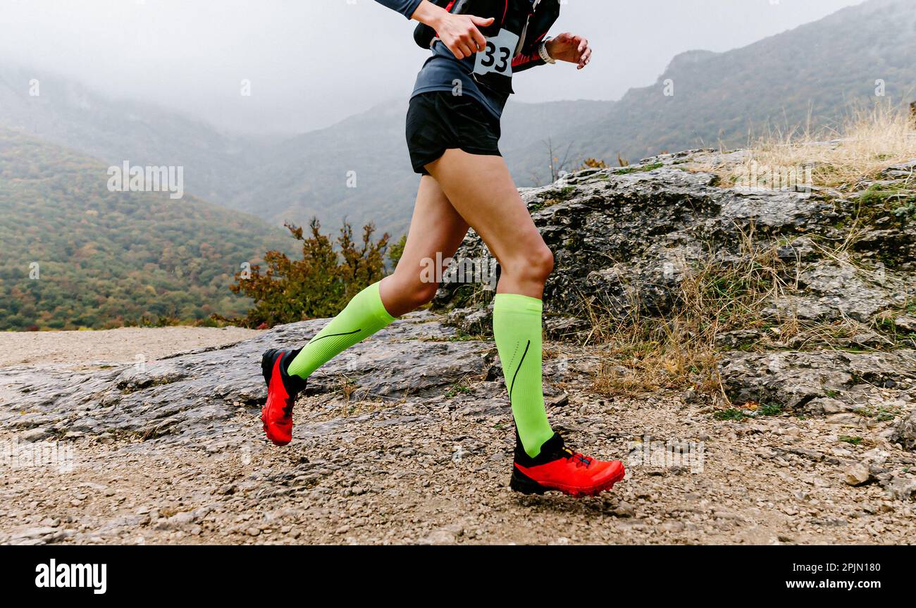 atleta femminile in calze a compressione corsa di montagna pista, jogging in autunno tempo nebbia attraverso il terreno montuoso Foto Stock