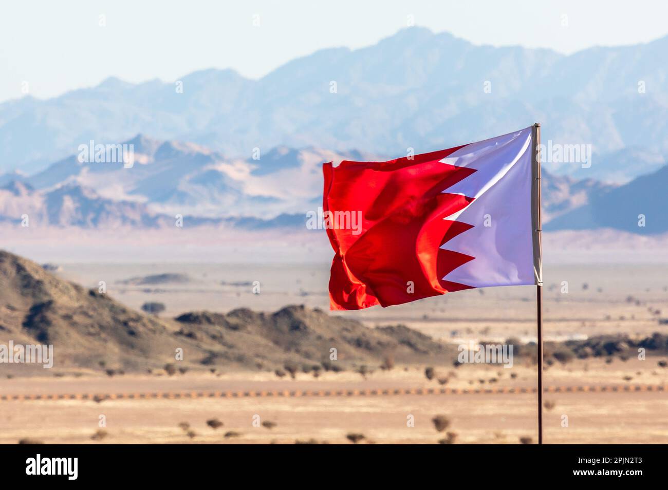 Bandiera del Bahrain che sventola sul vento nel deserthwith Saudita montagne sullo sfondo, al Ula, Arabia Saudita Foto Stock