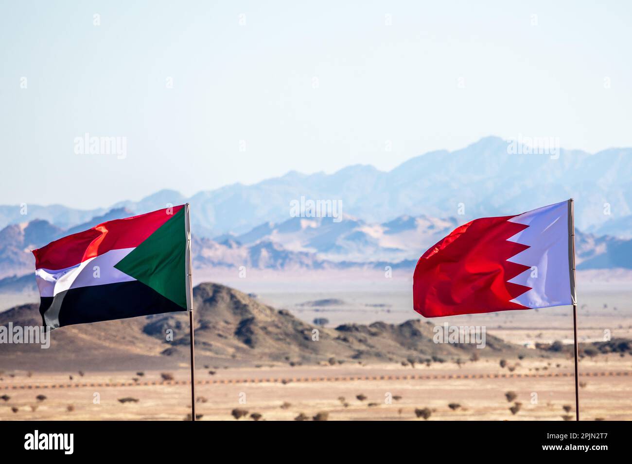 Bandiere sudanesi e del Bahrain che sventolano sul vento in desertsaudacon montagne sullo sfondo, al Ula, Arabia Saudita Foto Stock