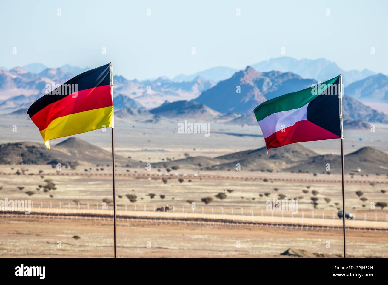 Bandiere tedesche e kuwaitane che sventolano sul vento nel deserto dell'Arabia Saudita con montagne sullo sfondo, al Ula, Arabia Saudita Foto Stock