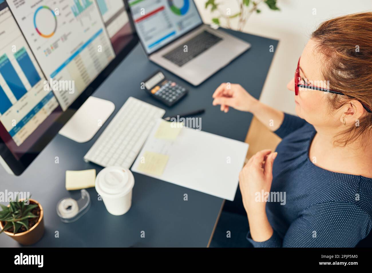 Donna d'affari che lavora con dati finanziari su grafici e tabelle sul computer. Imprenditore donna che guarda i diagrammi e le statistiche seduto alla scrivania in ufficio Foto Stock