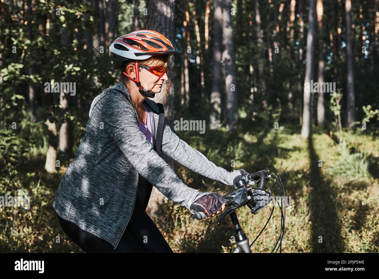 Donna attiva in bicicletta su strada forestale. Donna in bicicletta in fuoristrada percorso durante il giorno delle vacanze estive. Donna che indossa casco e guanti da bicicletta Foto Stock