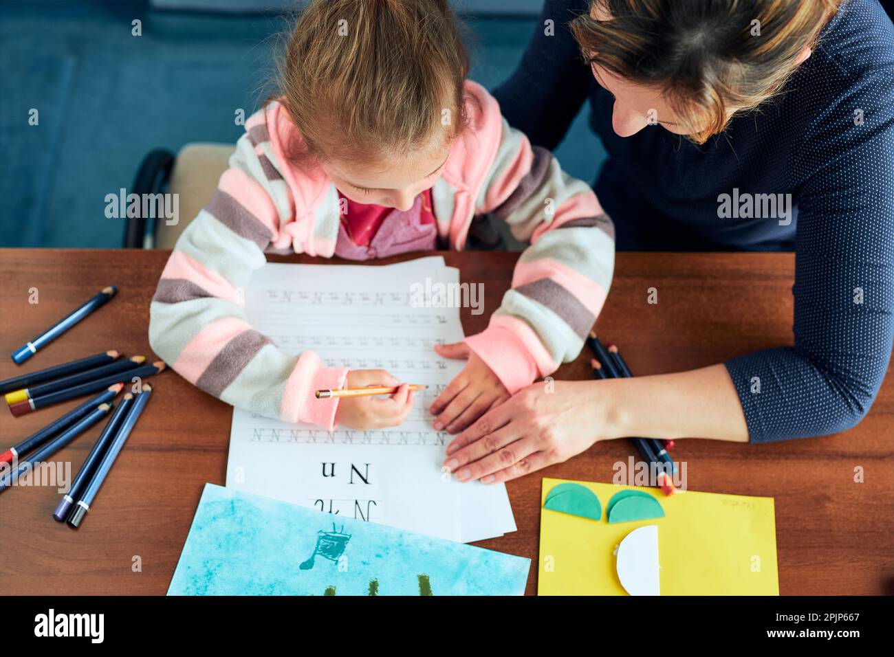 Bambina che impara a scrivere lettere con l'aiuto di sua madre. Ragazzo che scrive lettere, disegna immagini, fa cose con la carta Foto Stock