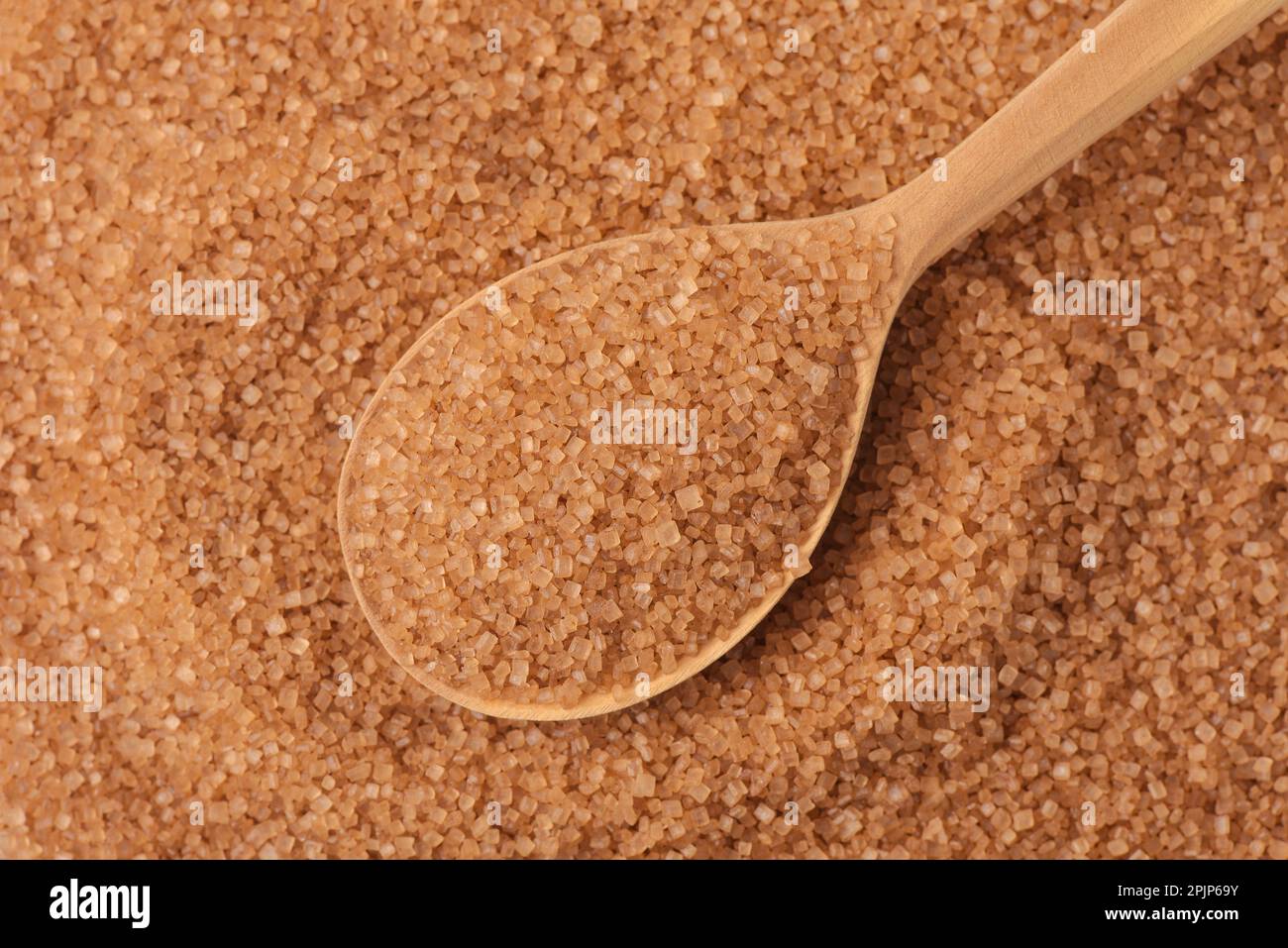 Vista dall'alto del cucchiaio di legno sullo sfondo di zucchero di canna marrone granulato Foto Stock