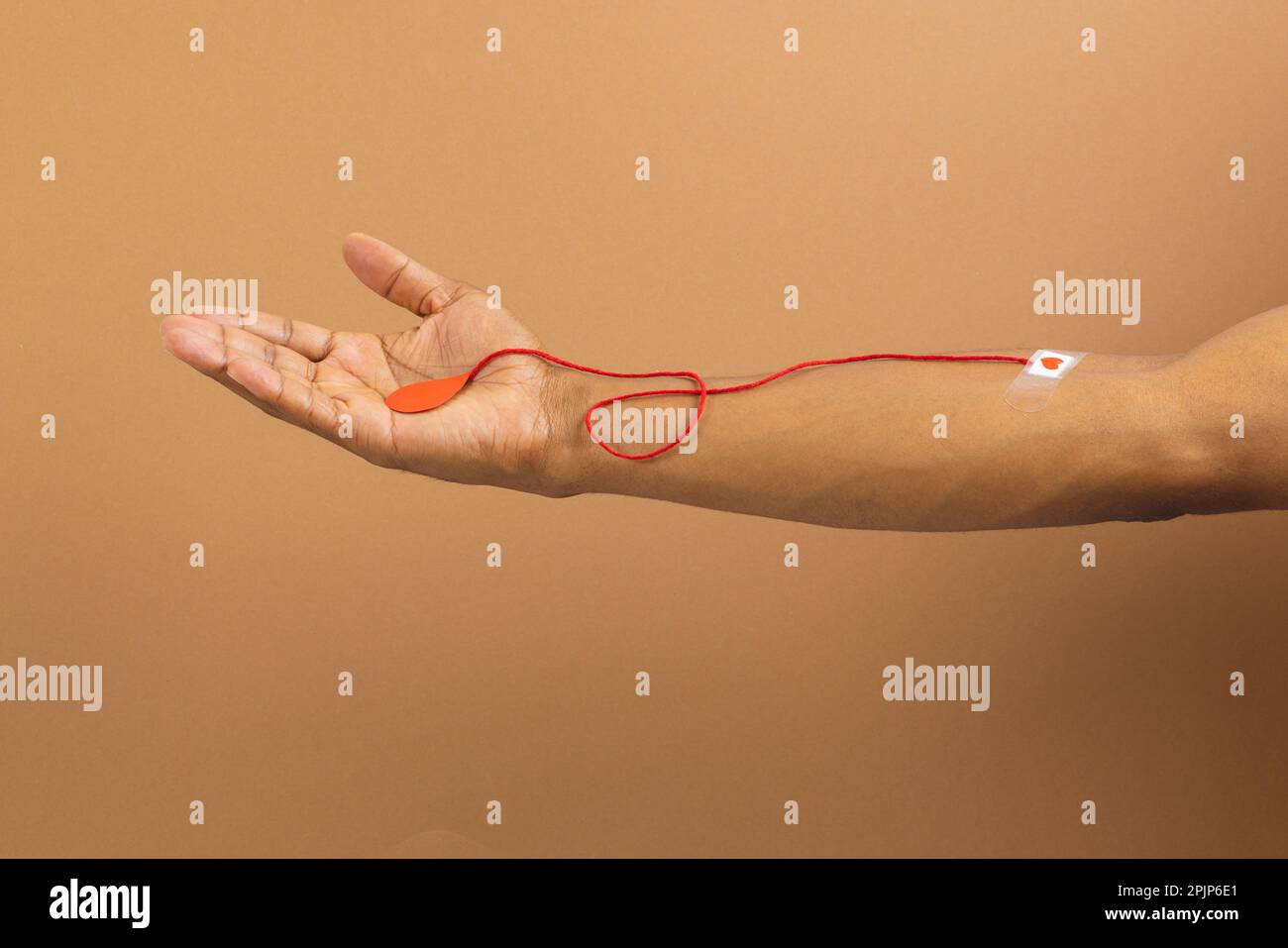 Braccio di uomo biraciale con cerotto che si attacca al cuore e corda rossa con goccia di sangue, su fondo marrone Foto Stock