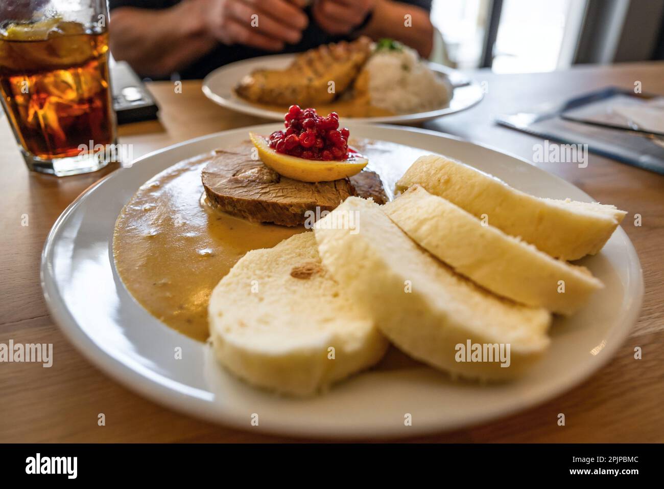 Gnocchi con salsa di sirloin (tradizionale 'vickova' di cibo ceco) con mirtilli rossi e filetto di manzo su piatto, limonata, parte di mangiare uomo, ristorante. Foto Stock