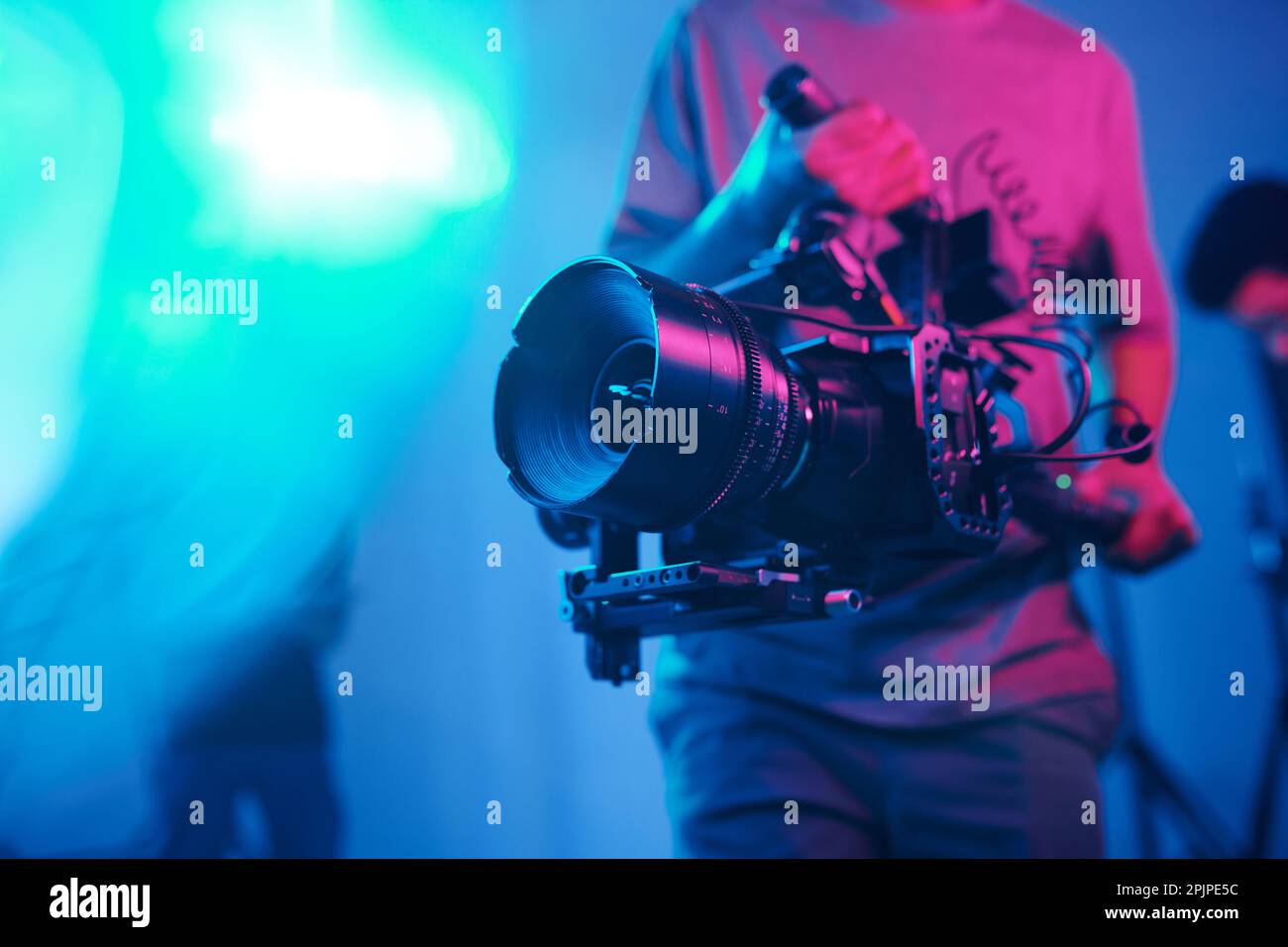 Primo piano delle riprese di un giovane cameraman con una fotocamera professionale mentre si eseguono contenuti in studio Foto Stock