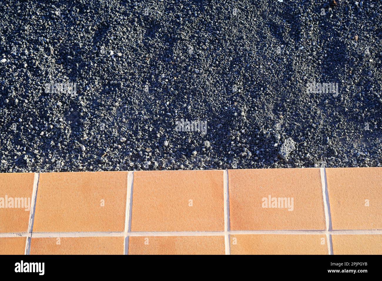 Pacciame da giardino in ghiaia nero vulcanico e bordo di patio piastrellato utilizzato per eleganti giardini minimalisti. Febbraio 2023. Foto Stock