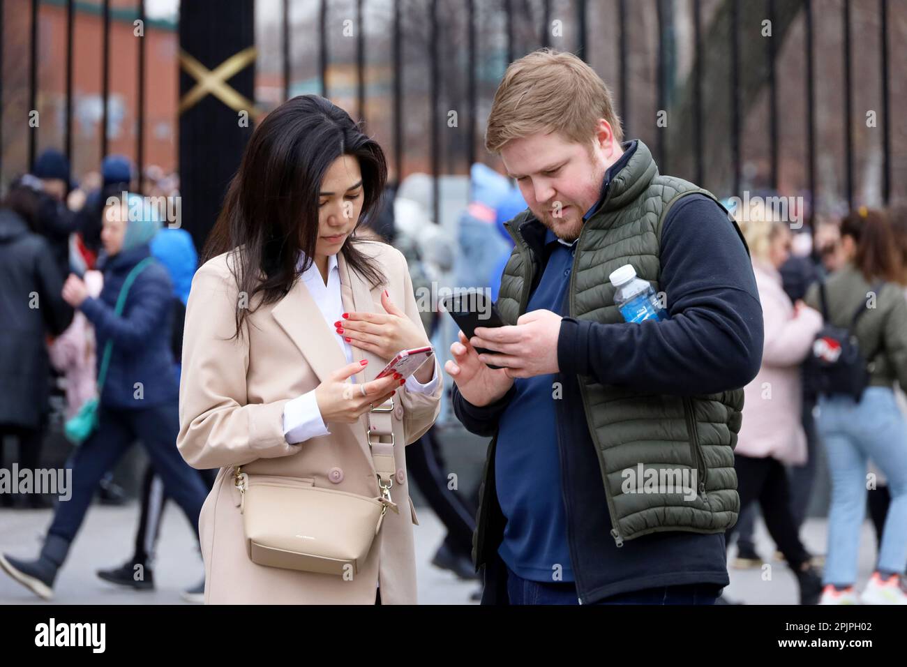 Coppia in piedi con gli smartphone su una strada, donna asiatica e uomo caucasico nella città di primavera Foto Stock