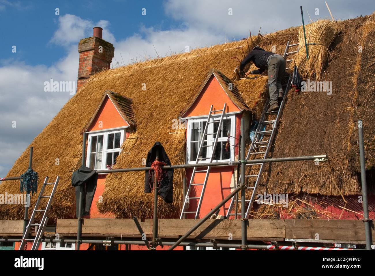Osserva un maestro Thatcher al lavoro, mentre posa con cura un nuovo portello su un classico tetto di cottage britannico, una scena senza tempo di vita rurale. Foto Stock