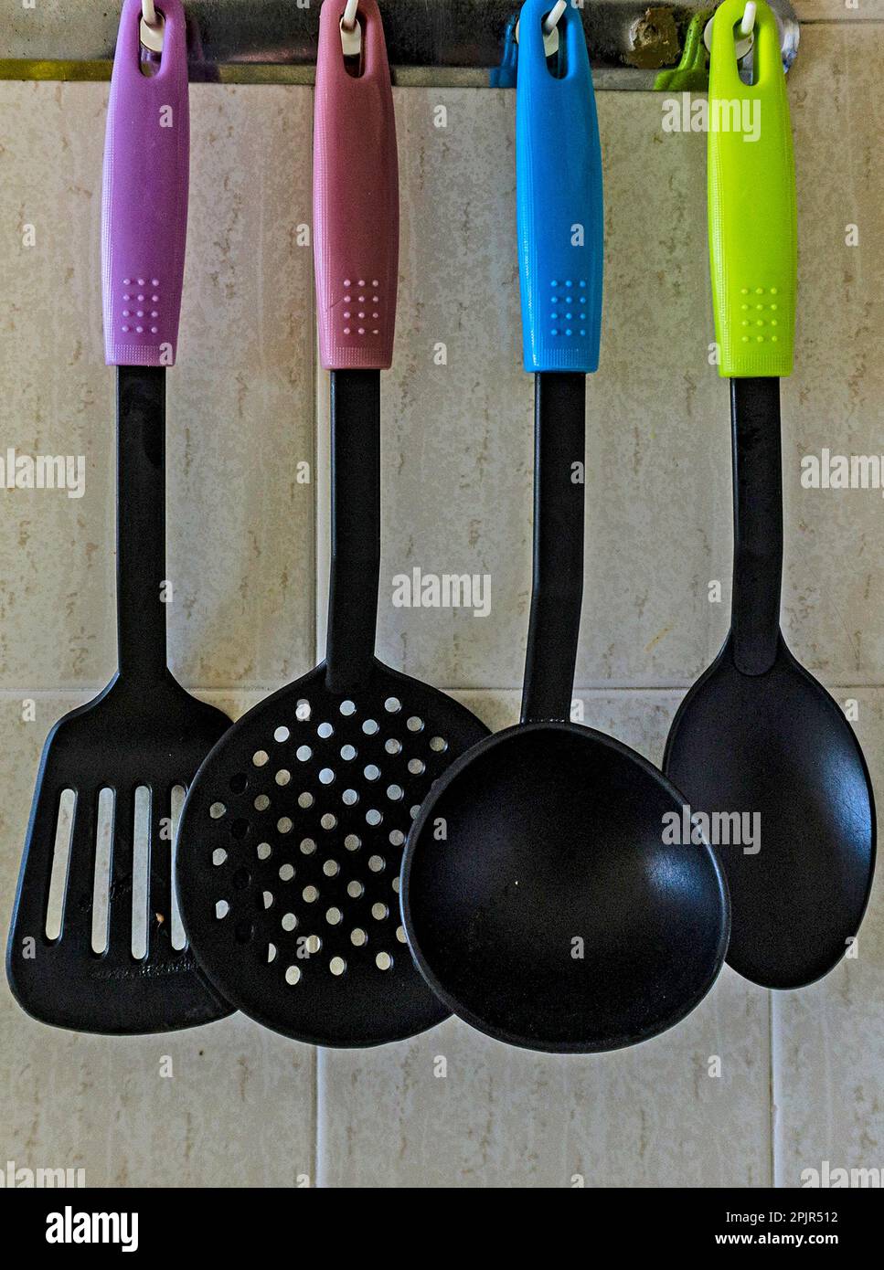 Quattro utensili da cucina colorati appesi su una parete della cucina. Foto Stock