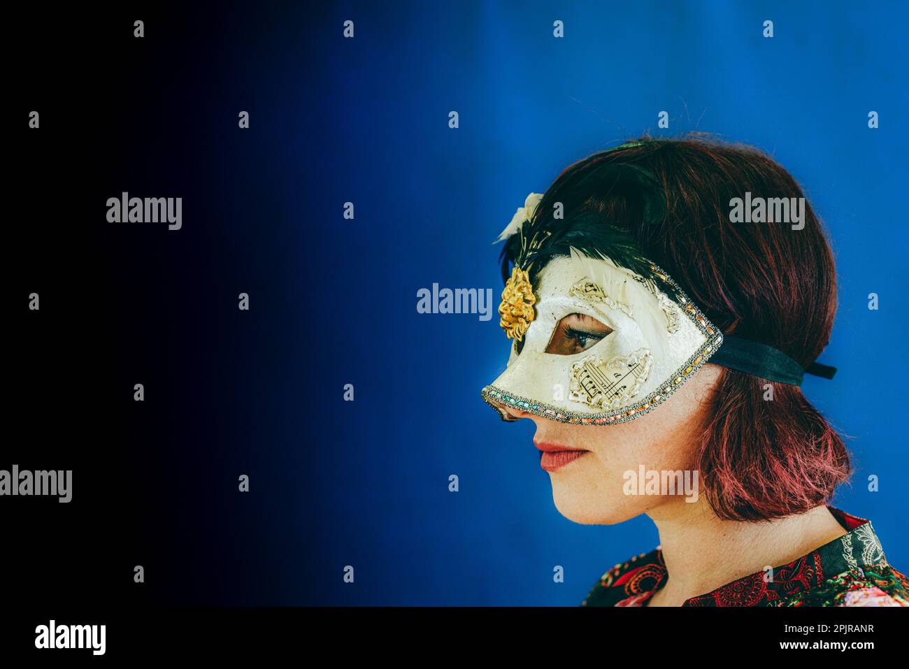 Ritratto di una donna adulta con testa rossa caucasica che indossa una maschera teatrale veneziana, studio spara terra blu con messa a fuoco selettiva Foto Stock