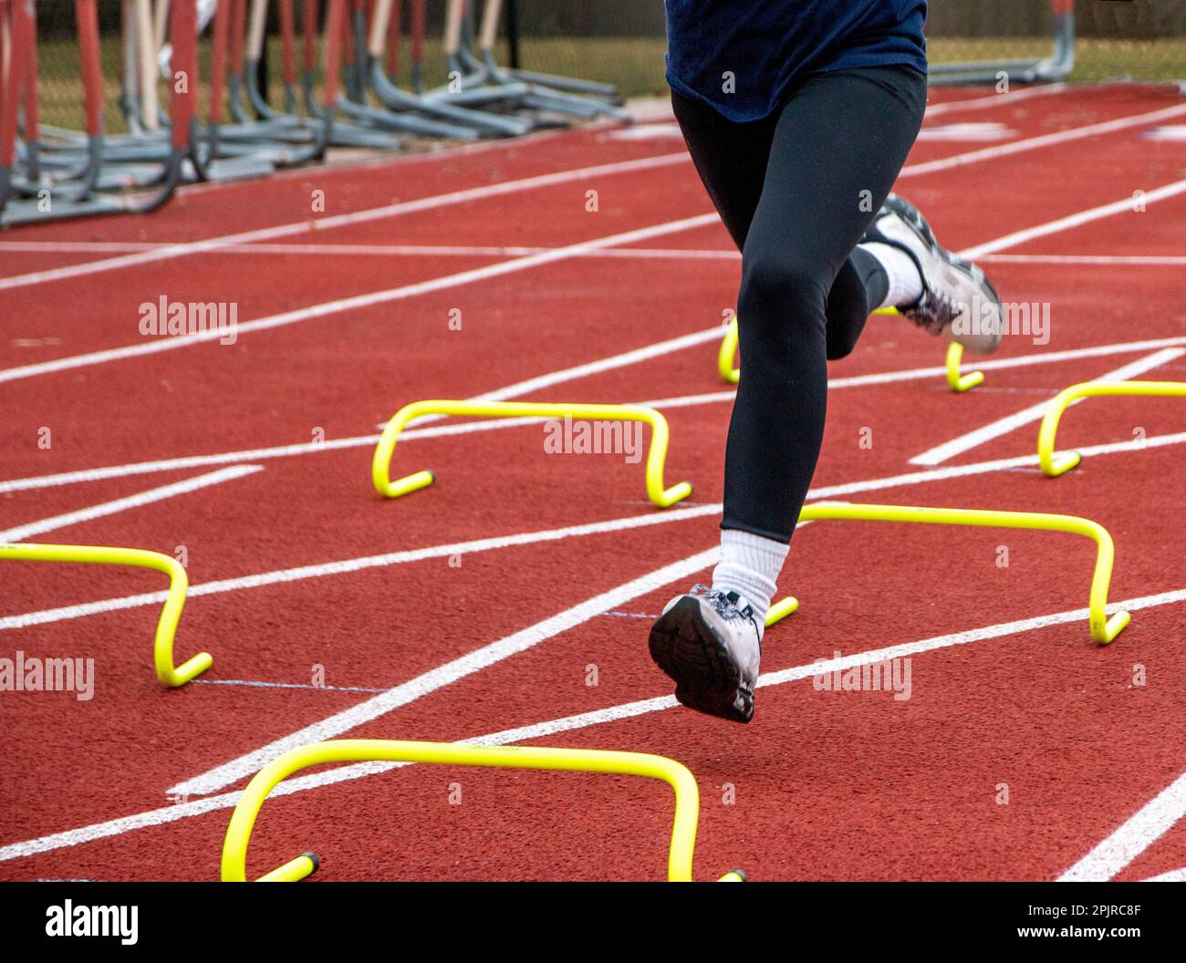 Un runner gambe indossare spandex nero che corre oltre sei pollici giallo banana ostacoli in corsia su una pista durante la pratica. Foto Stock