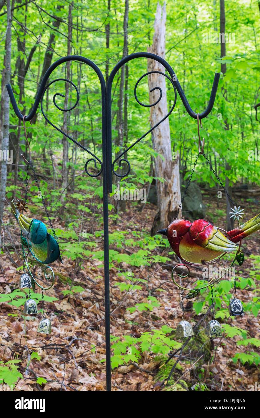 Fumetti colorati in metallo dipinto uccelli vento appesi su ferro battuto nero stand in foresta di alberi decidui nel giardino cortile in primavera. Foto Stock