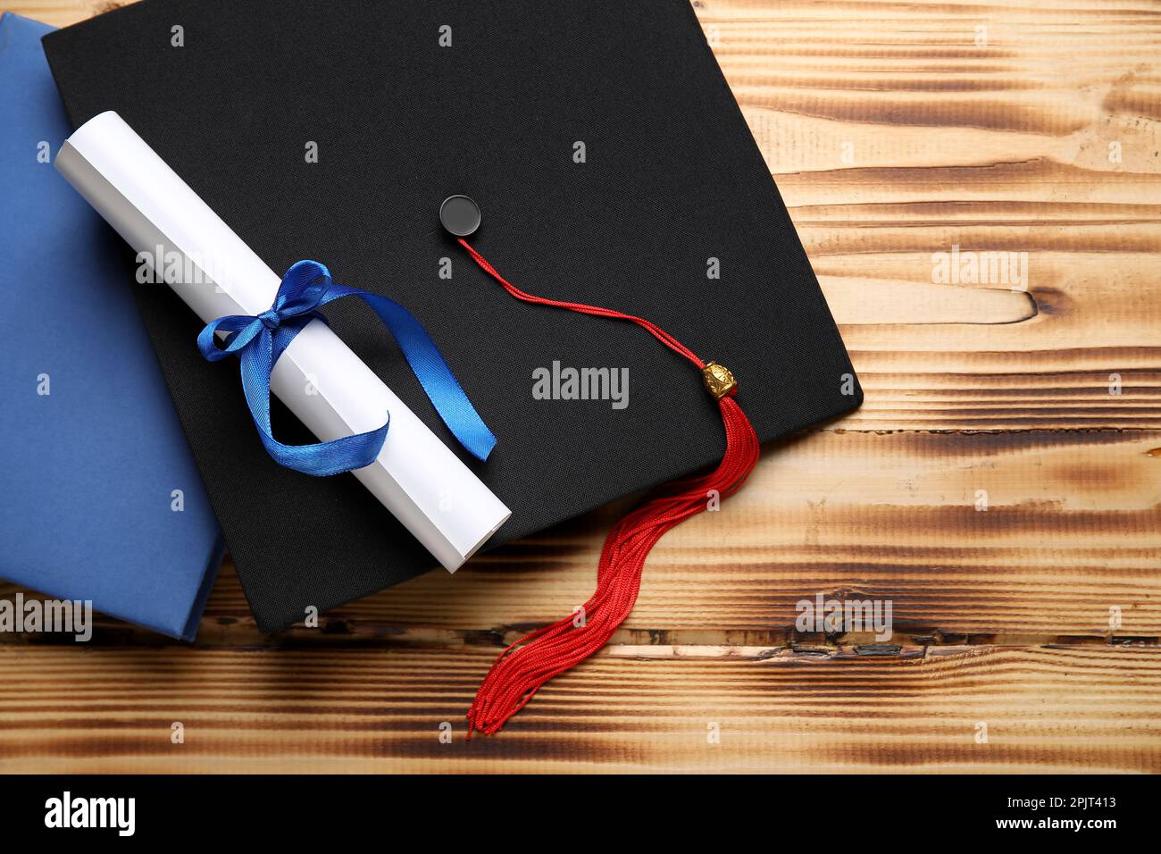 Diploma con nastro blu, cappello di laurea e libro su tavolo di legno Foto Stock