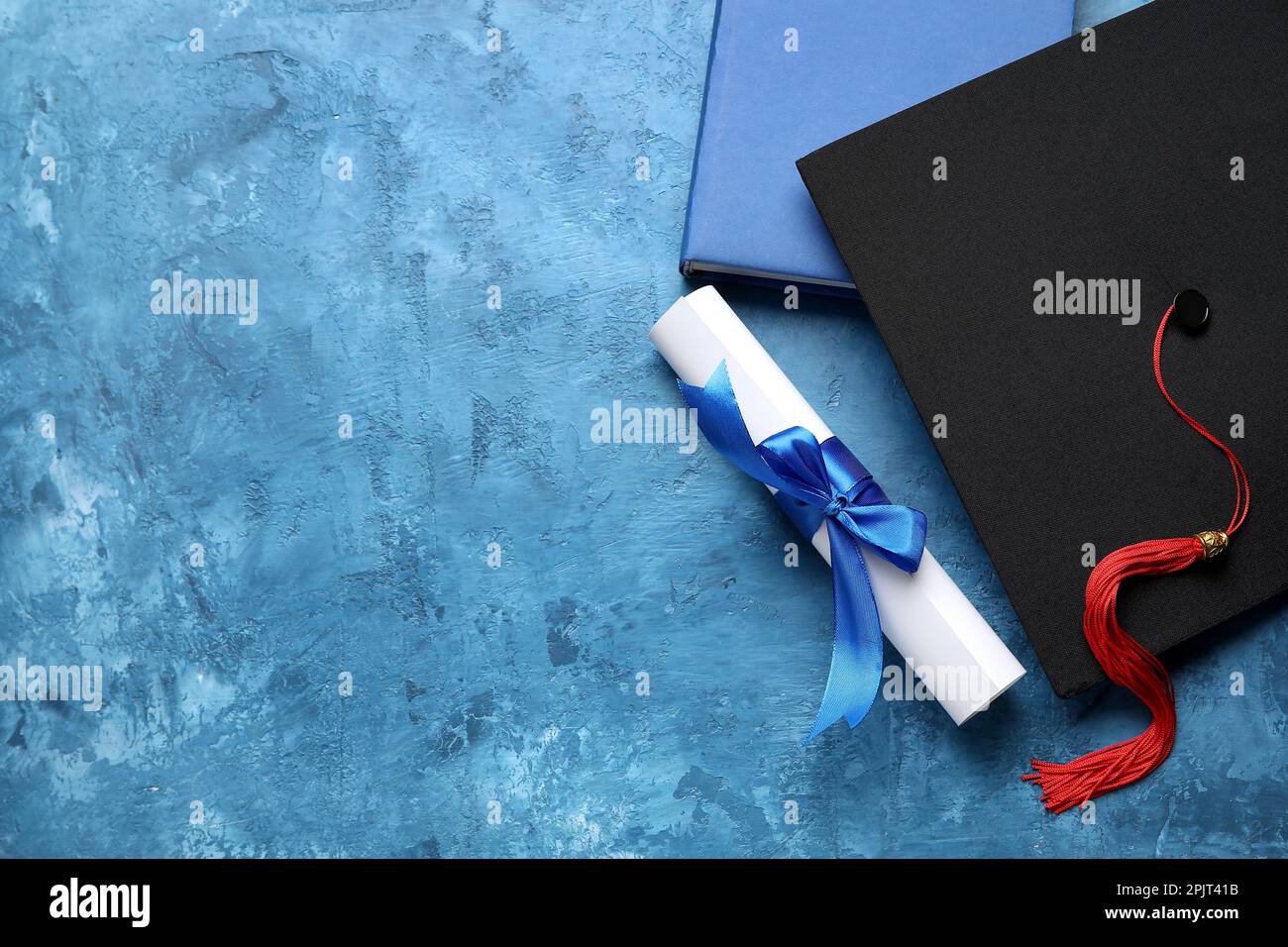 Diploma con nastro, cappello di laurea e libro su tavolo blu Foto Stock