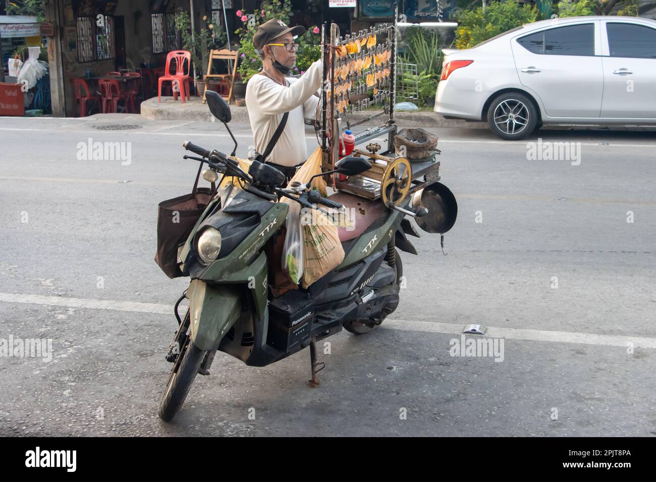 SAMUT PRAKAN, THAILANDIA, MAR 24 2023, Un fornitore regola calamari essiccati pressati su un supporto montato su una motocicletta Foto Stock