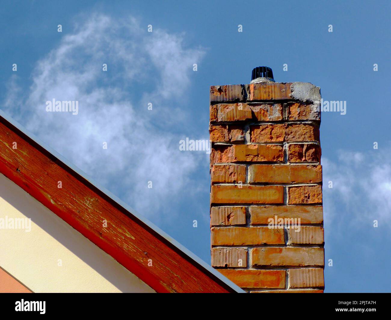 Camino isolato in mattoni di argilla deteriorante con intemperie, superficie di spalling. rivestimento in legno sulla parete di fine della casa a timpano. stucco bianco elevazione esterna. Foto Stock