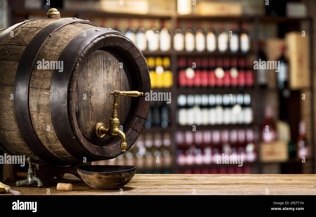 Barilotto con rubinetto in rame e bottiglie di vino sugli scaffali sullo sfondo. Foto Stock