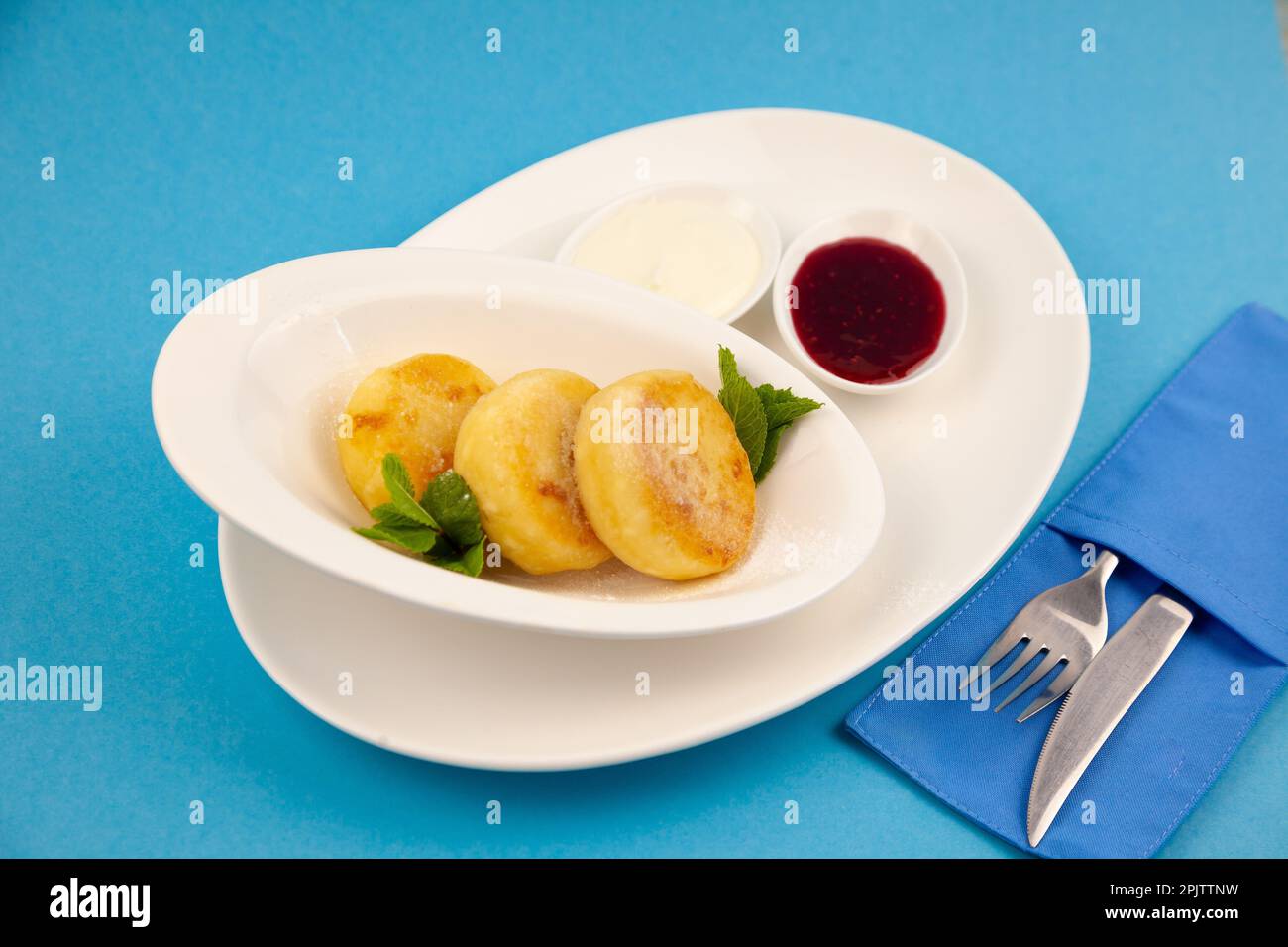 Frittelle di formaggio ricotta rotonda in un piatto bianco su sfondo blu. Cibo prima colazione. Cibo sano. Salsa di panna acida e menta. Primo piano vista dall'alto. Pasto dessert. Frittelle di ricotta al formaggio ricotta. Foto Stock