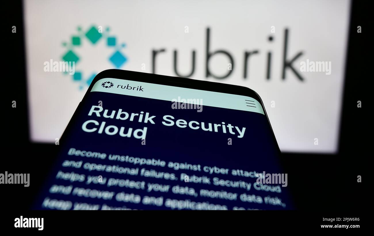 Smartphone con sito Web di Rubrik Inc., azienda statunitense che si occupa della sicurezza dei dati, sullo schermo di fronte al logo aziendale. Messa a fuoco in alto a sinistra del display del telefono. Foto Stock