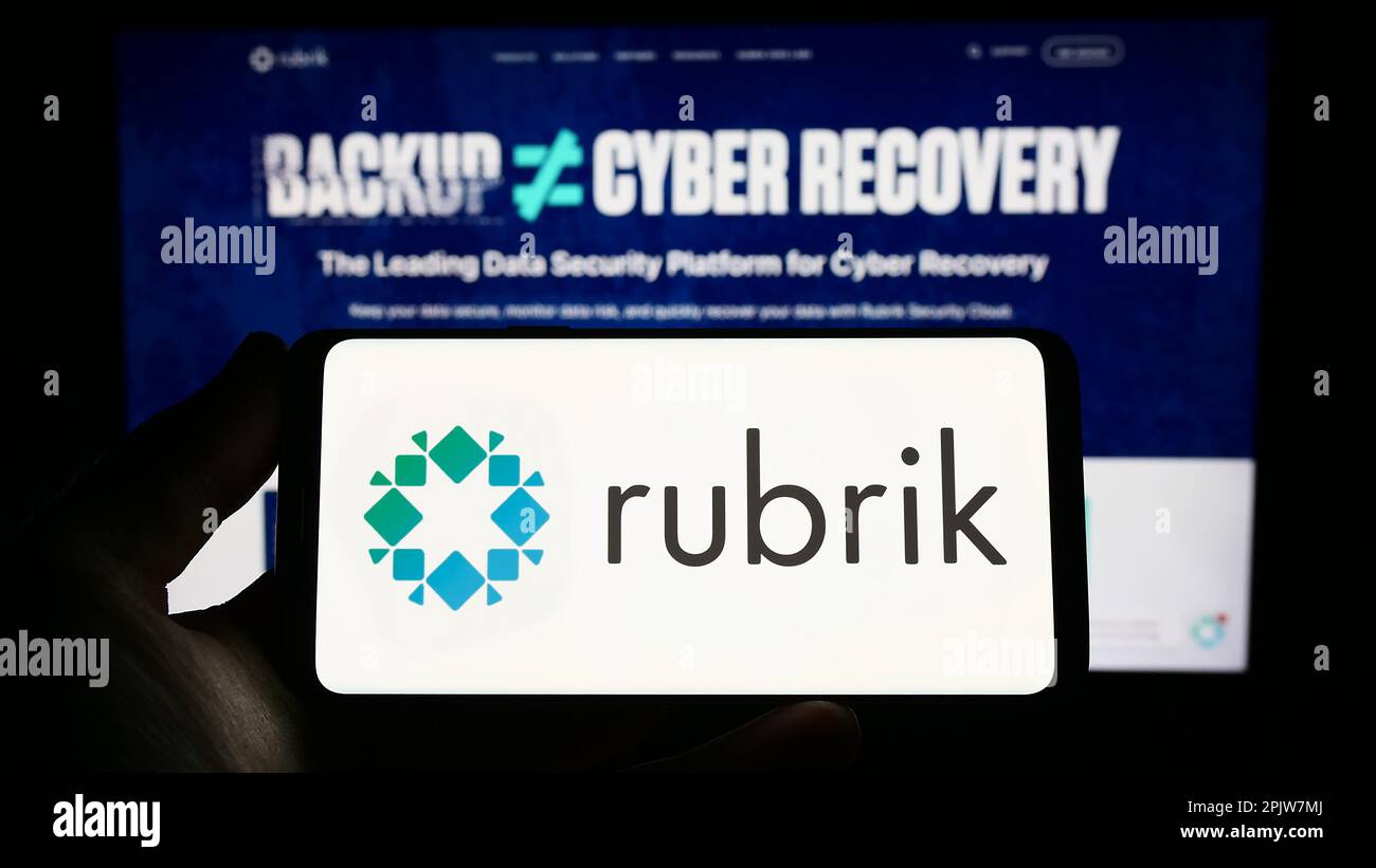 Persona che tiene in mano uno smartphone con il logo della società di sicurezza dei dati statunitense Rubrik Inc. Sullo schermo di fronte al sito Web. Messa a fuoco sul display del telefono. Foto Stock