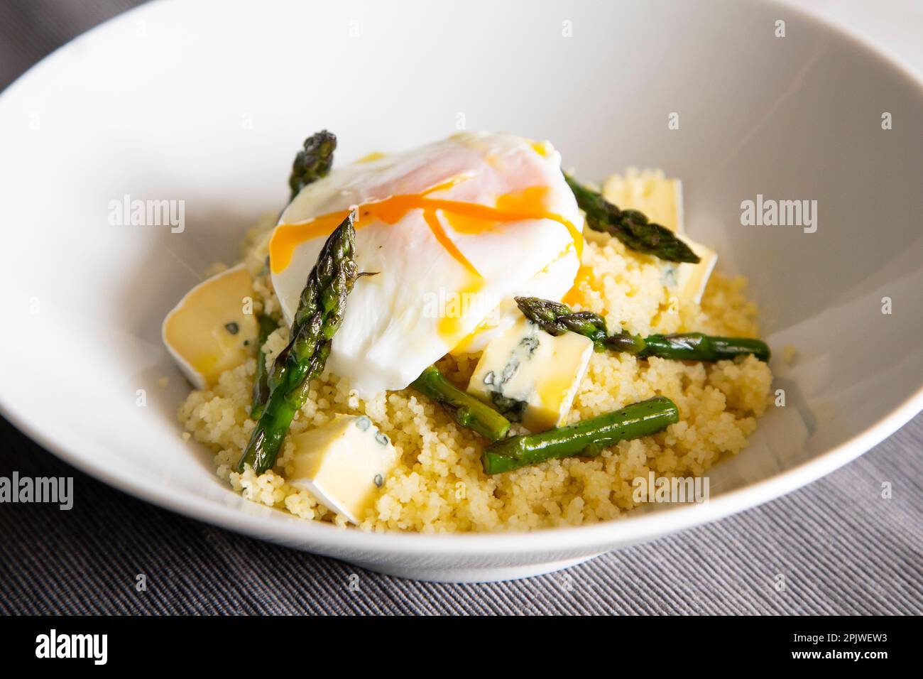 Couscous piatto con un uovo fritto, asparagi verdi e formaggio blu. Foto Stock