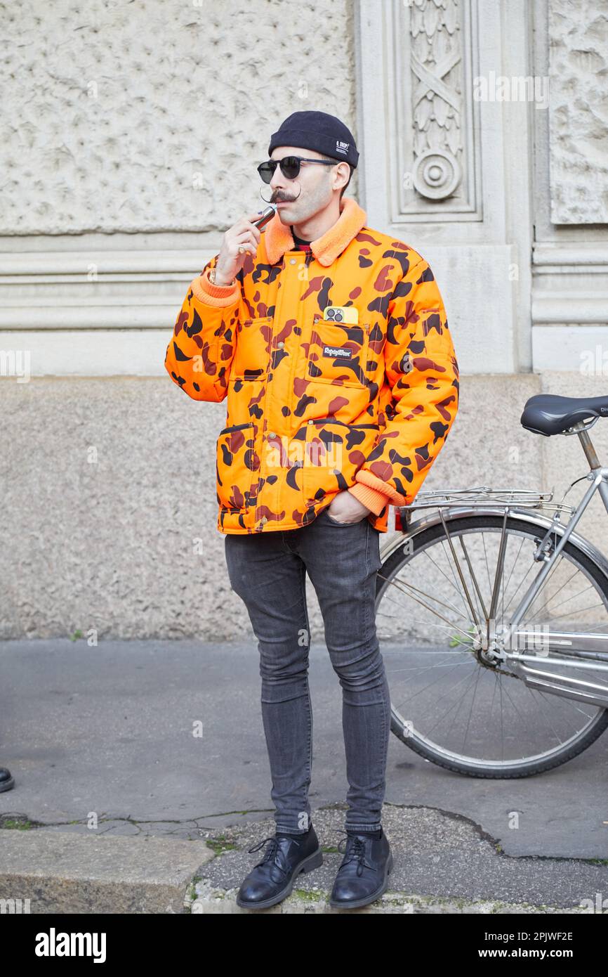 MILANO, ITALIA - 25 FEBBRAIO 2023: Uomo con giacca imbottita refrigerata arancione e pantaloni in denim grigio prima della sfilata Missoni, Milano Fashion Week st Foto Stock