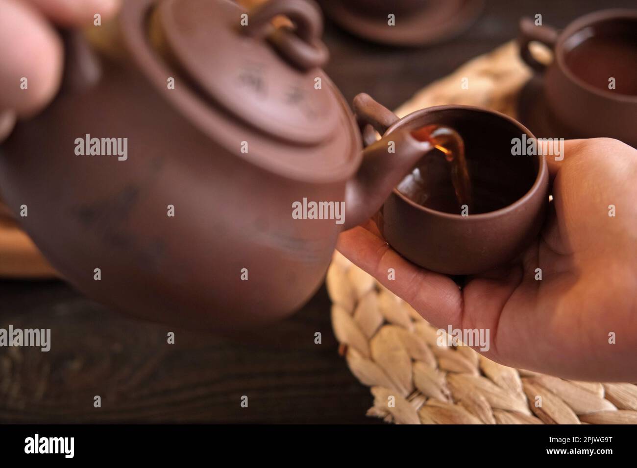 Cerimonia del tè. Tradizionale utensile da tè asiatico, che serve un autentico set. Persona che versa il tè dalla teiera di ceramica marrone a Teacup. Vassoio di bambù. Stile di vita. Noi Foto Stock