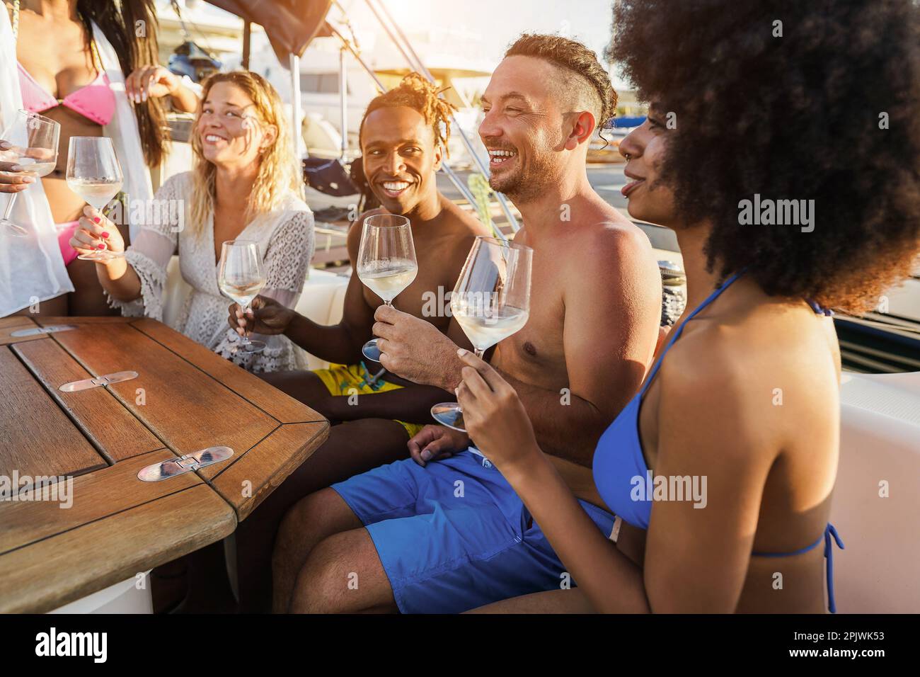 Amici multirazziali felici che hanno vino bevente divertente alla festa della barca all'aperto - fuoco sulla mano destra che tiene il vetro Foto Stock