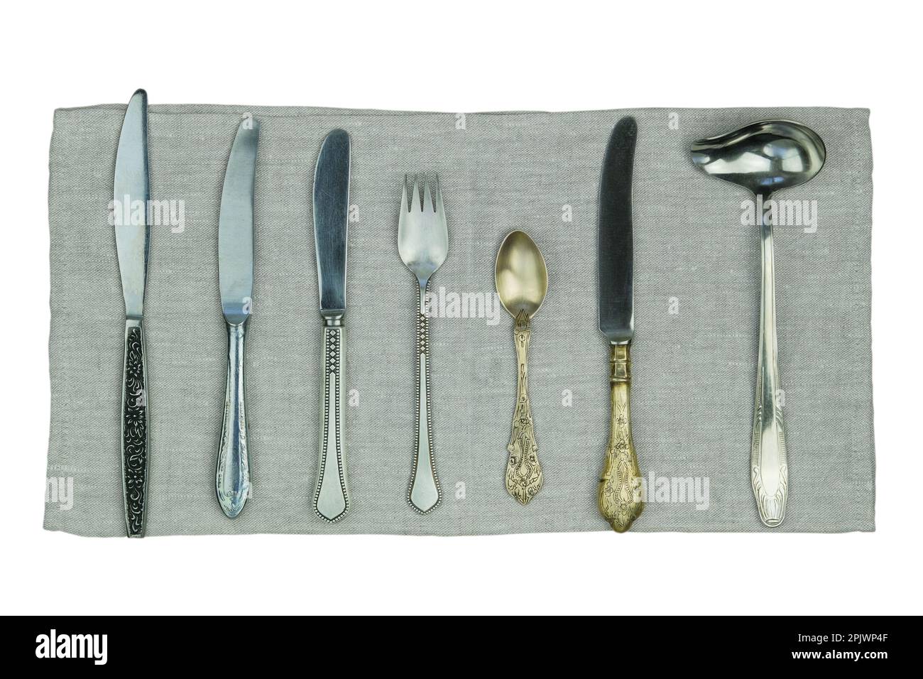Varietà di coltelli, forchette e altri utensili da cucina su un tovagliolo di lino isolato su uno sfondo bianco. Vista dall'alto. Foto Stock