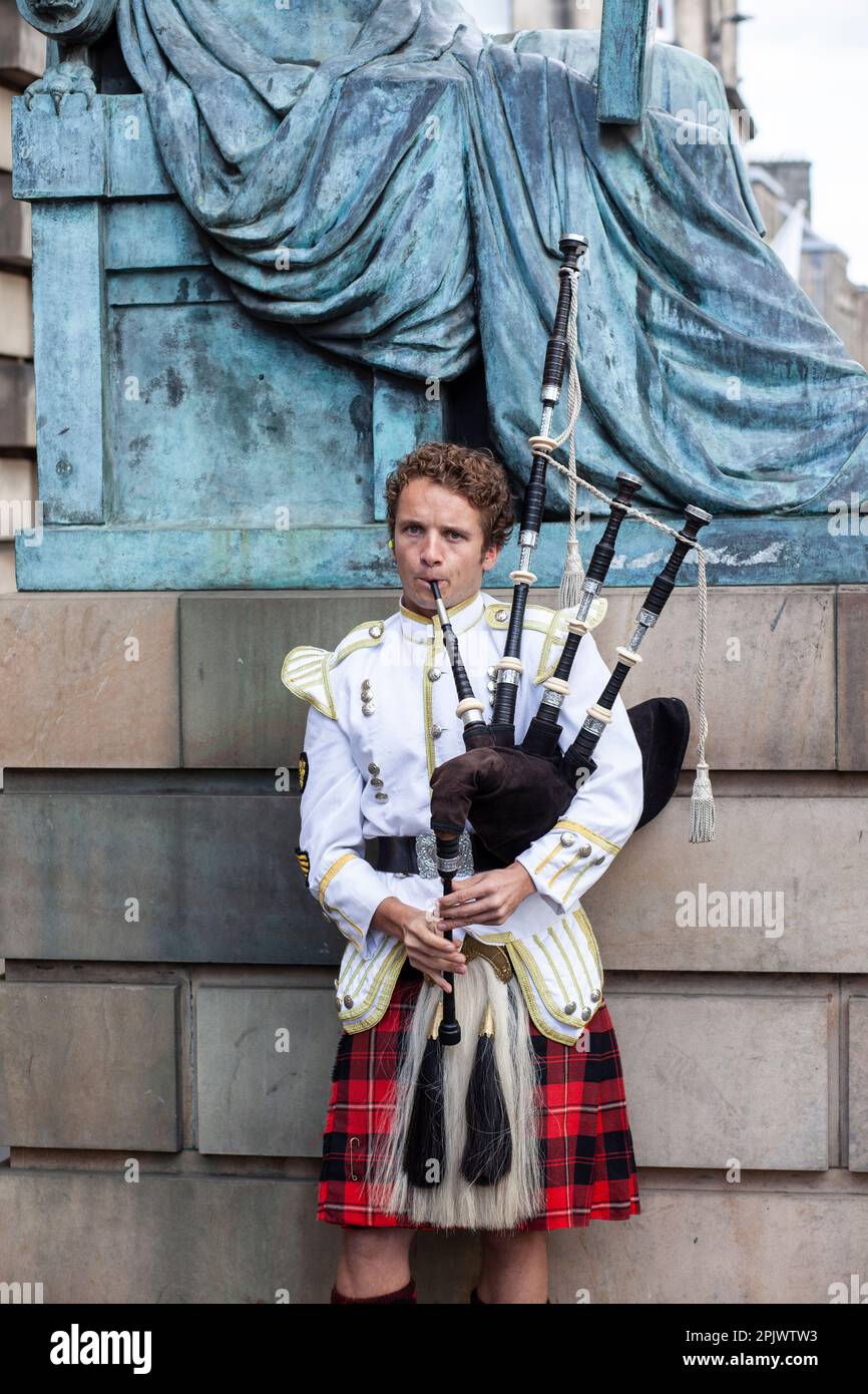 -Edinburgh,Scotland 16 ottobre 2015 il bagpiper scozzese, vestito con tradizionale abito tartan rosso e nero, si trova davanti al muro di pietra. Edimburgo, la maggior parte Foto Stock