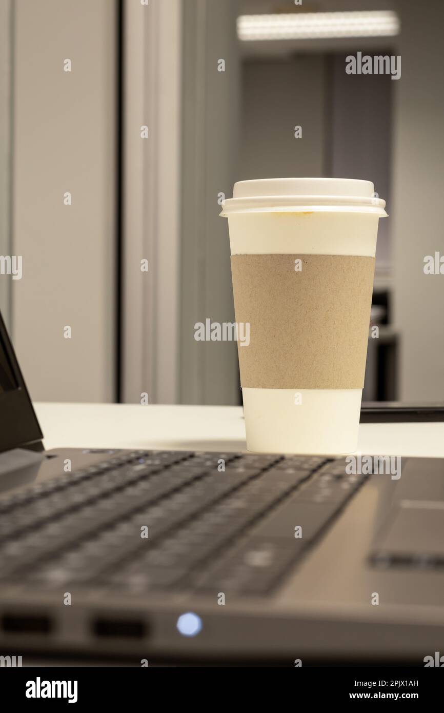 Tazza di caffè marrone e bianco usa e getta e un computer portatile Foto Stock