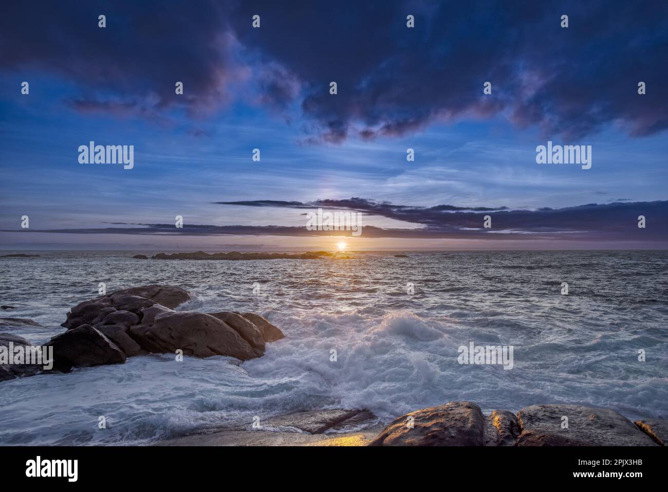 Tramonto su alcune barriere coralline battute dalle onde sulla costa galiziana della Spagna con pesanti nuvole d'acqua Foto Stock