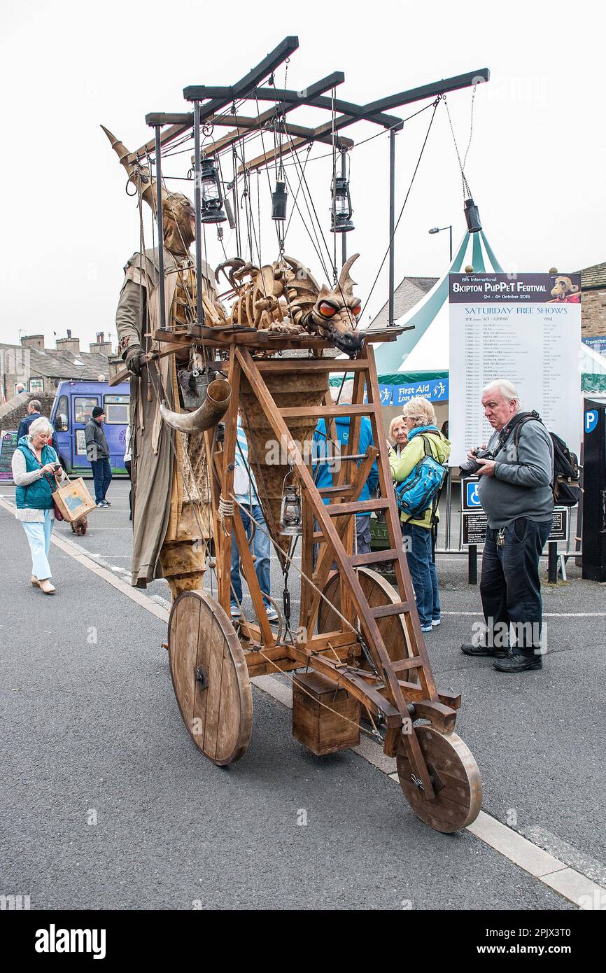 Persona su palafitte con un contraption mobile che sport un drago di respirazione del fuoco, visto al festival internazionale dei burattini di Skipton circa 2015. Foto Stock